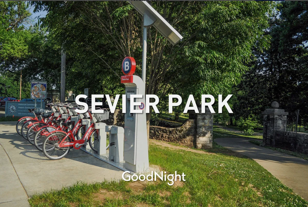 Sevier Park’s sign stands beside a convenient bicycle rental station amid lush greenery, hinting at energetic outdoor activities. The surrounding landscape invites families and groups to gather, bike, walk, or picnic.