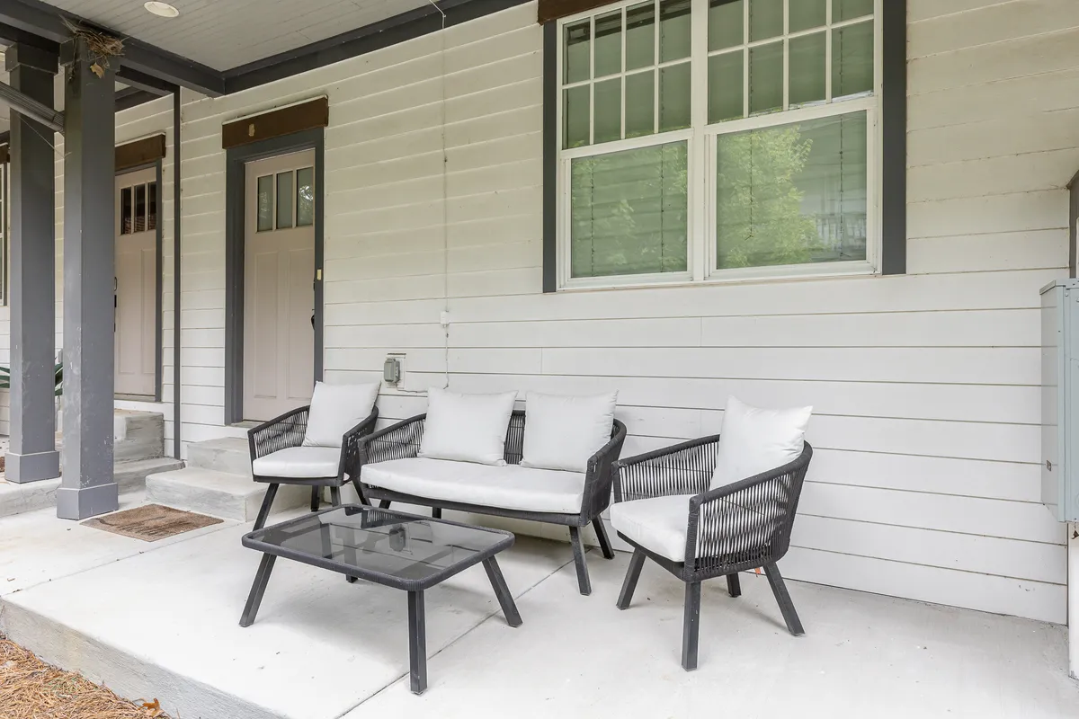 This image shows a cozy exterior porch with wicker seating and a glass coffee table, set against the backdrop of a front porch entry. The relaxed arrangement encourages friendly conversation and outdoor relaxation.