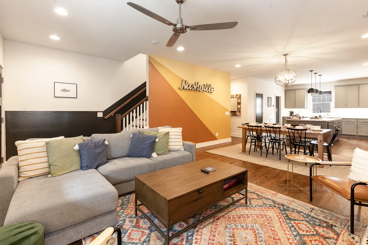 This image showcases a stylish, homey interior with a sofa, coffee table, visible dining area, and colorful wall art. The space is designed for socializing, dining, and entertaining, with an overall welcoming and flexible layout.