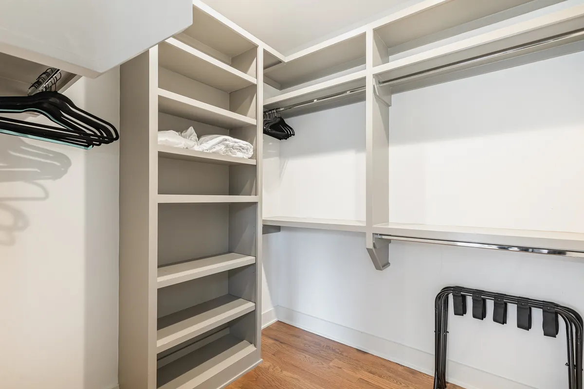 A minimalist walk-in closet with open shelving, hanging space, and a wooden floor, designed for efficient storage and easy organization. The uncluttered design promotes relaxation and order.