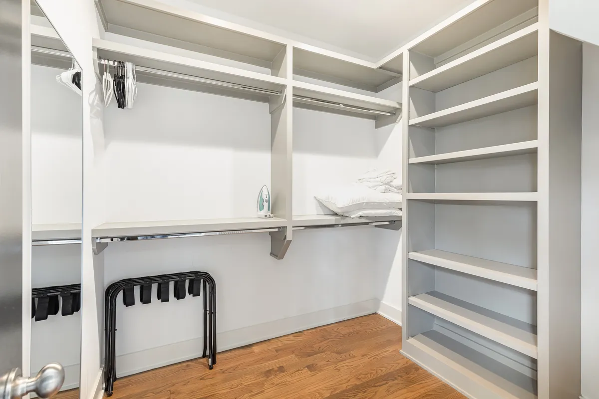 A tidy clothing storage zone with a hanging clothes rack, shelves, ironing board, and neatly folded towels. The cleanliness and organization support household functionality.