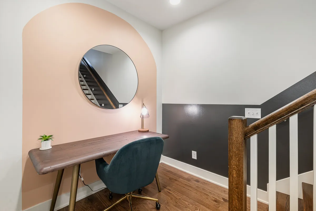 A contemporary workspace featuring a sleek desk with a task lamp, round mirror, and a green plant. The area is well-lit and designed to foster focus, making it ideal for remote work or study sessions.